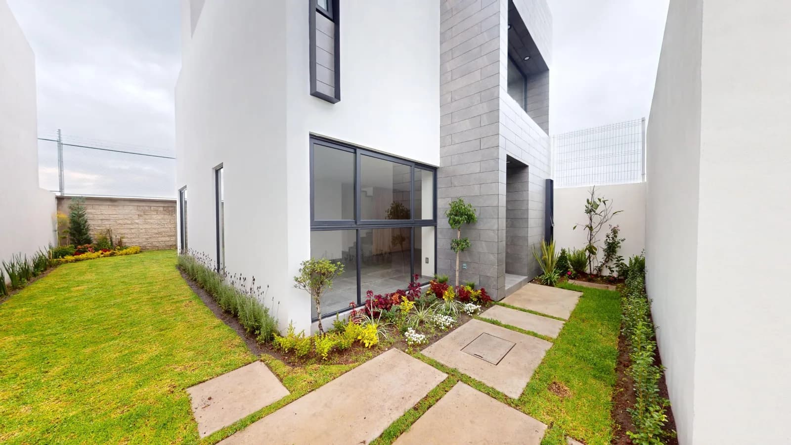 Jardín privado con andador de concreto y ventanal hacia la planta baja